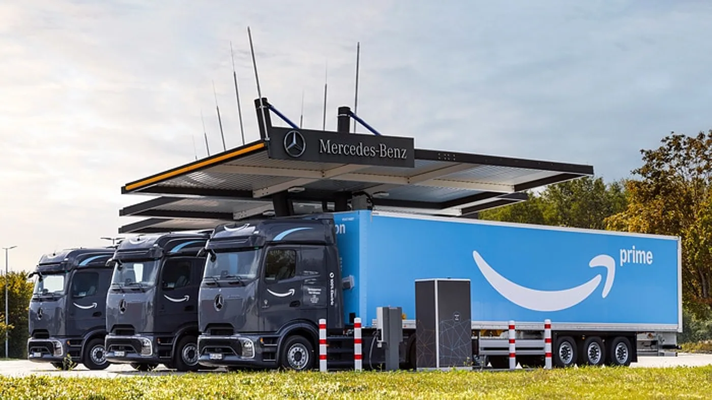 Mercedes-Benz eActros oscuros junto a un semirremolque azul Amazon en el exterior de una instalación