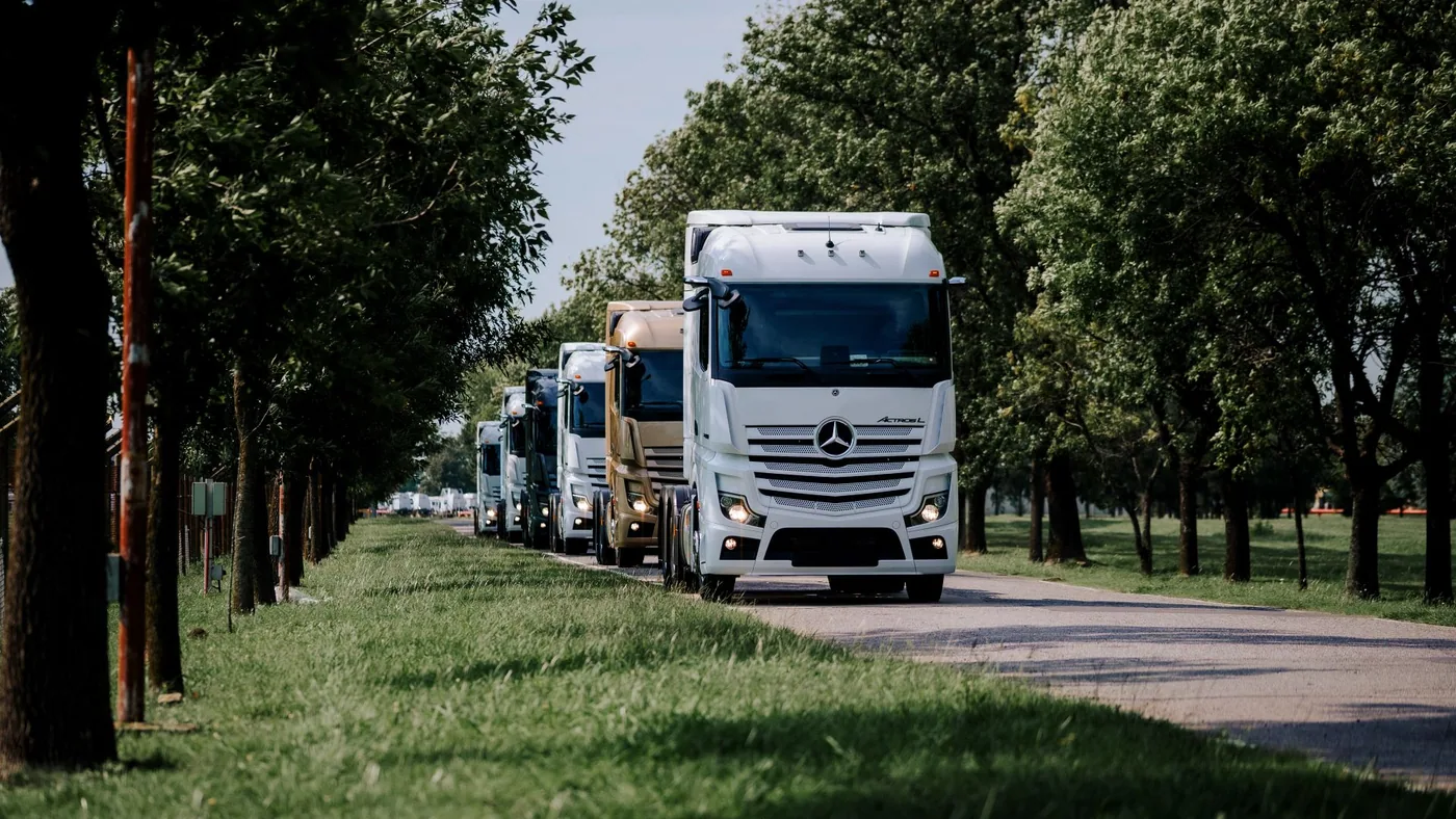 Caravana de camiones Mercedes-Benz en un camino arbolado