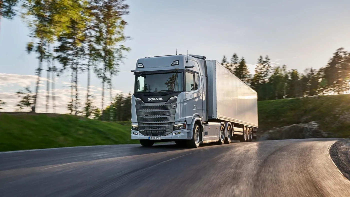 Scania Dynamic gris con semirremolque circulando por una ruta arbolada