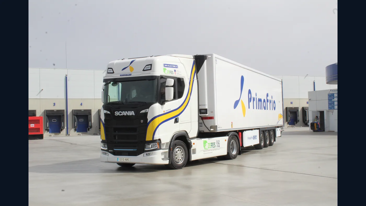 Tractora Scania eléctrica blanca con semirremolque Primafrio ante un centro logístico