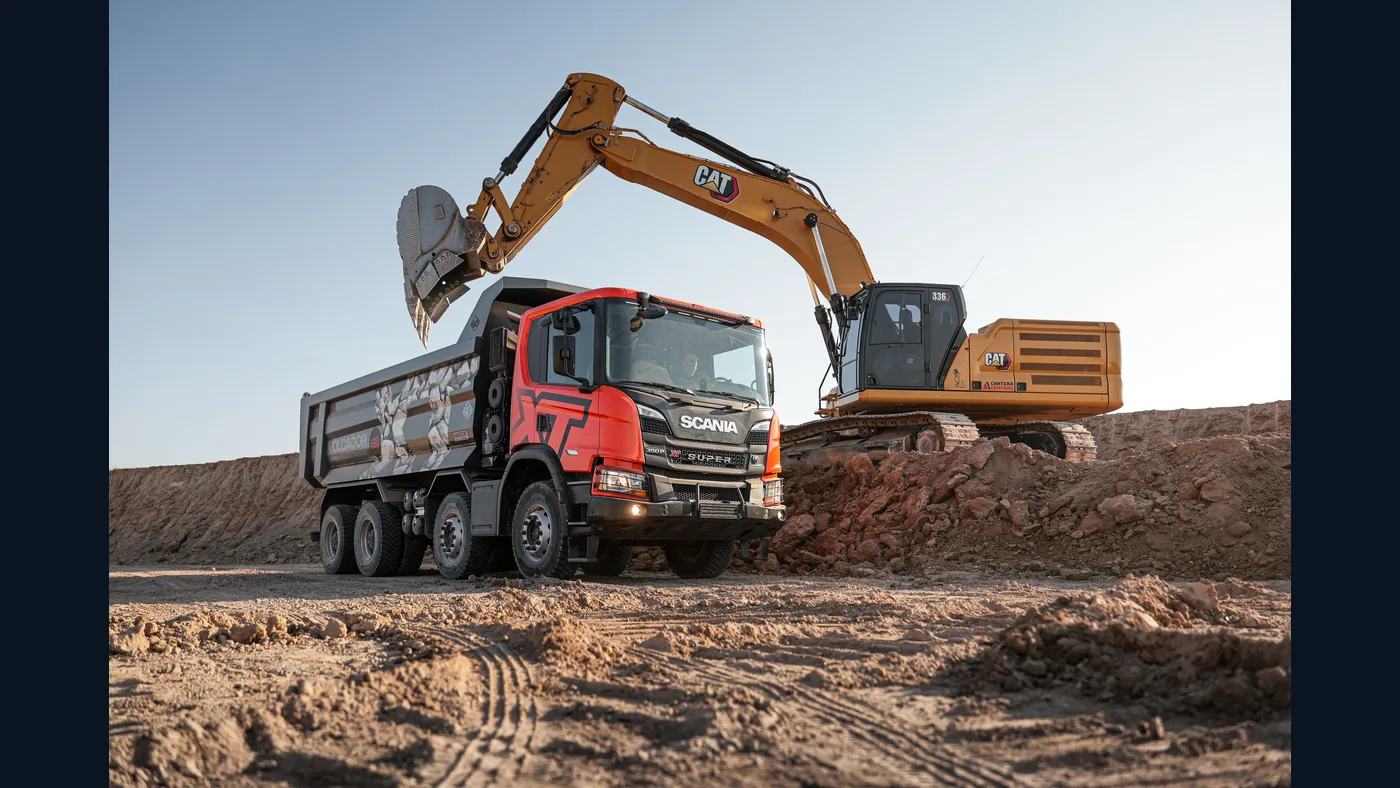 Camión volcador Scania rojo trabajando junto a una excavadora en una obra