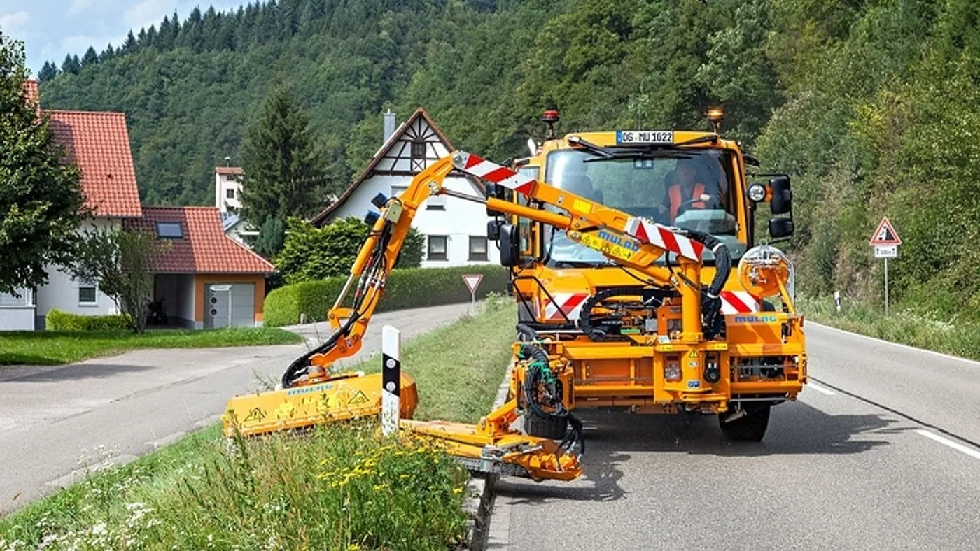 Unimog equipado con brazos y herramientas de corte trabajando en una banquina