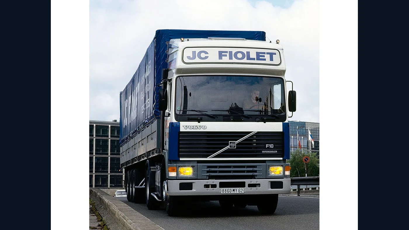 Camión Volvo F10 Intercooler blanco y azul circulando con carga y conductor visible